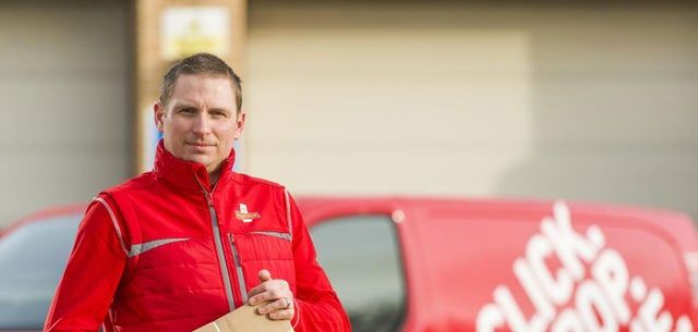 A Royal Mail delivery driver holding a parcel beside his van